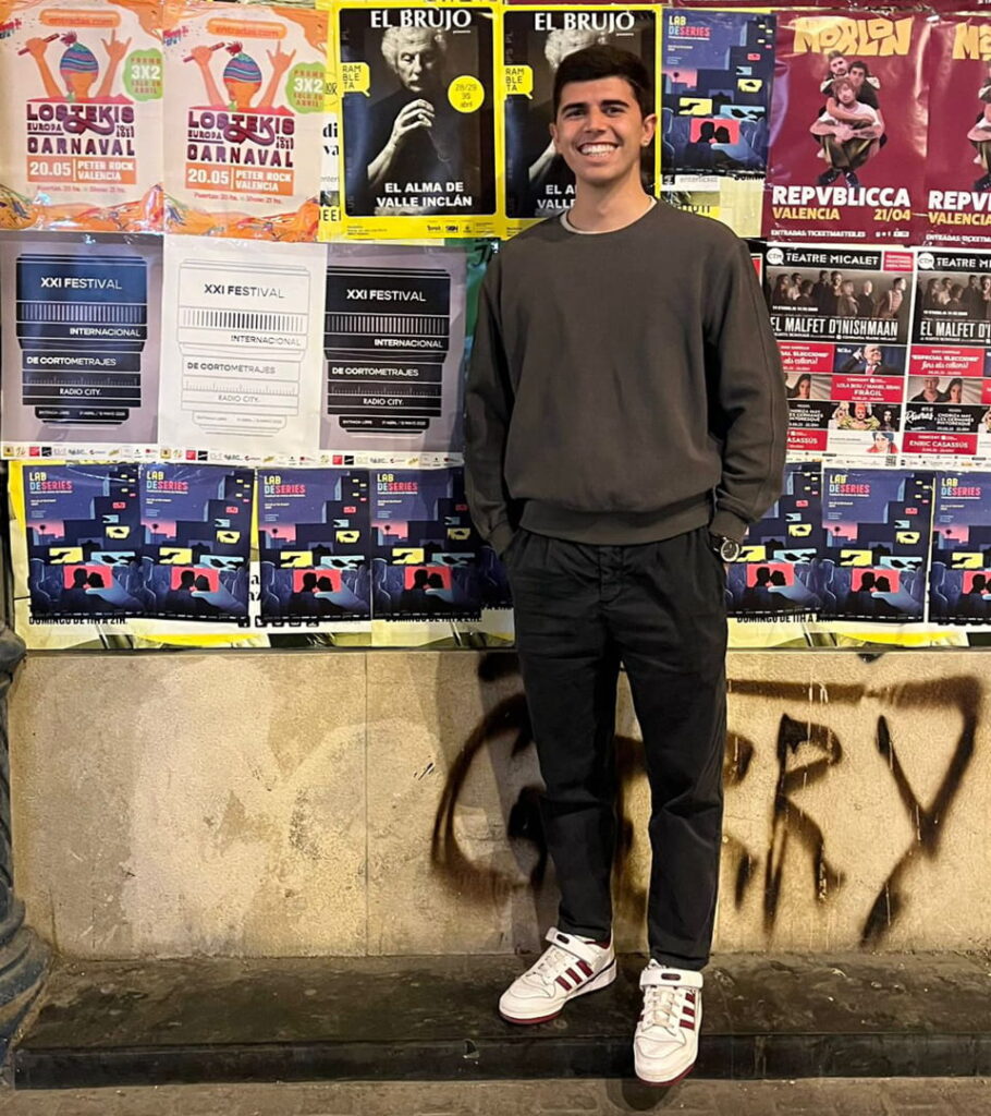Joan Sanchis sonriente posando frente a una pared cubierta de carteles de eventos, incluyendo varios del XXI Festival Internacional de Cortometrajes Radio City.