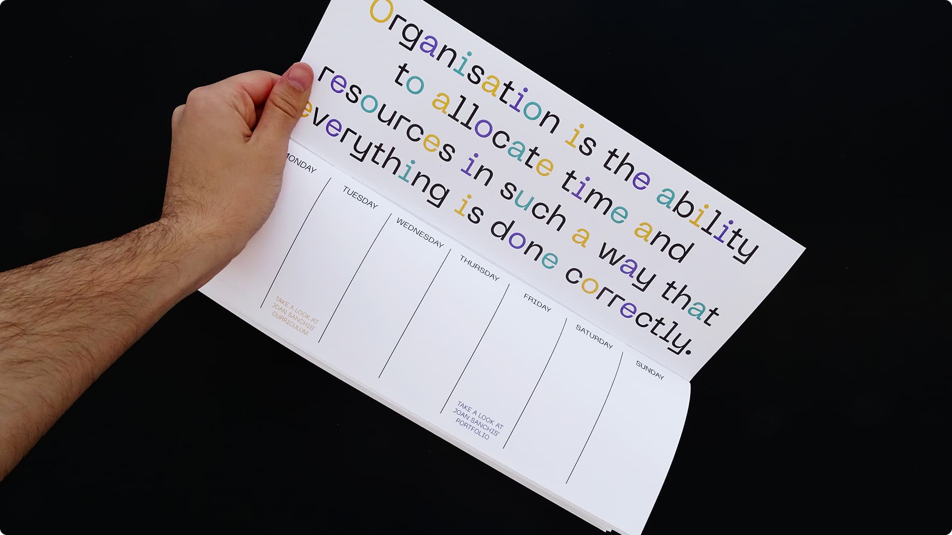 Mano pasando una página del planificador semanal abierto, mostrando una frase sobre organización en tipografía multicolor en la página