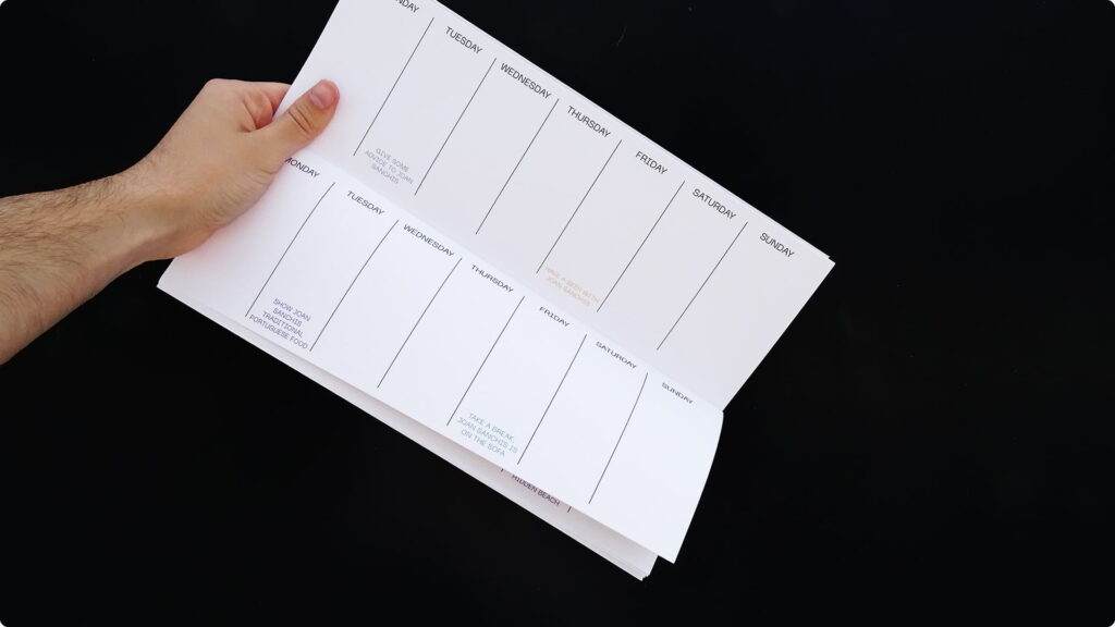 Mano pasando una página del planificador semanal, mostrando dos vistas de la cuadrícula interior con los días de la semana y espacio para anotaciones, sobre un fondo negro